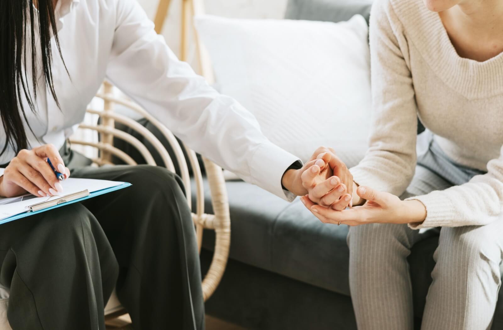 Two people sitting during a conversation; one offers support while holding the other's hand
