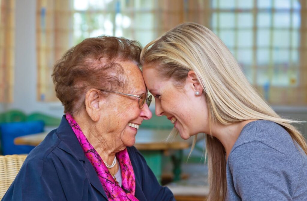 An adult grandchild presses their forehead against their grandparent’s as each smiles, showing connection amid dementia