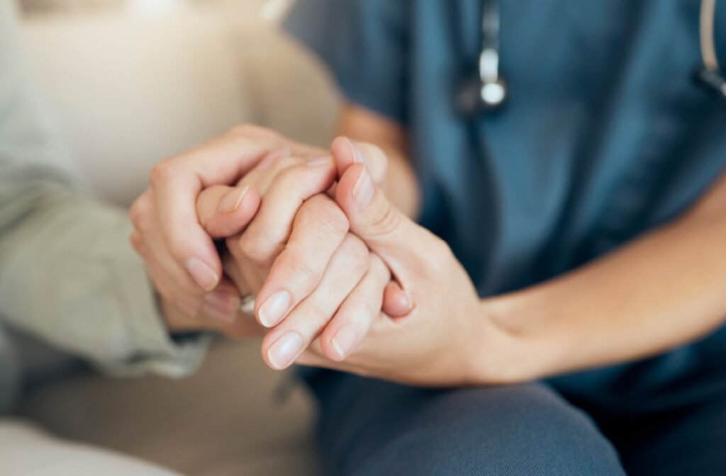close up of caregiver holding hands with a senior to support them in assisted living community.